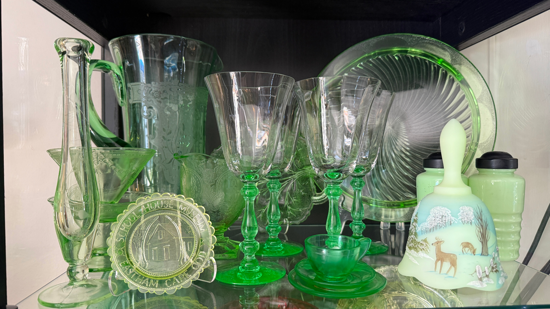 A shelf of vintage uranium glass — pitchers, goblets, plates, and a hand-painted bell